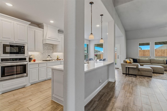 kitchen with oven, black microwave, light wood-type flooring, custom exhaust hood, and gas stovetop