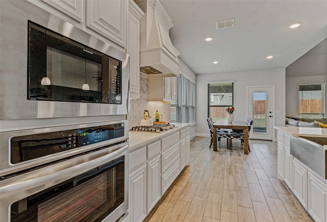 kitchen featuring premium range hood, tasteful backsplash, white cabinetry, appliances with stainless steel finishes, and light countertops