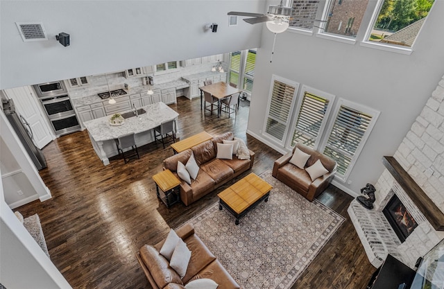 living room with a high ceiling, dark hardwood / wood-style flooring, ceiling fan, and a fireplace