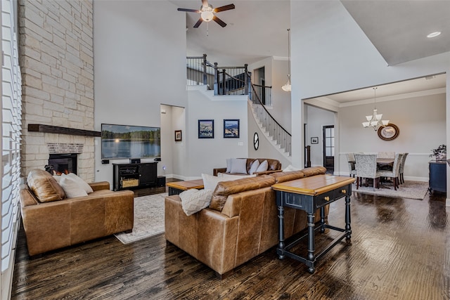 living room featuring a stone fireplace, ceiling fan with notable chandelier, dark hardwood / wood-style floors, and a high ceiling