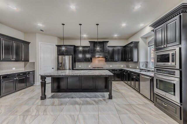 kitchen with tasteful backsplash, light stone counters, a center island, hanging light fixtures, and appliances with stainless steel finishes