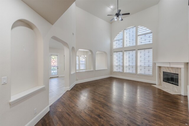 unfurnished living room featuring ceiling fan with notable chandelier, dark hardwood / wood-style flooring, high vaulted ceiling, and a premium fireplace