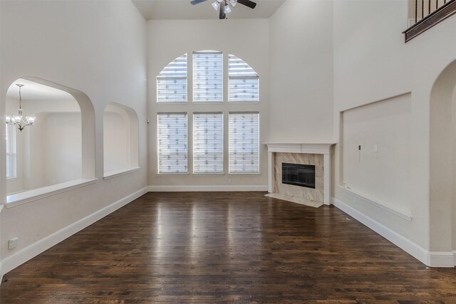 unfurnished living room with dark wood-type flooring, a towering ceiling, ceiling fan with notable chandelier, and a fireplace