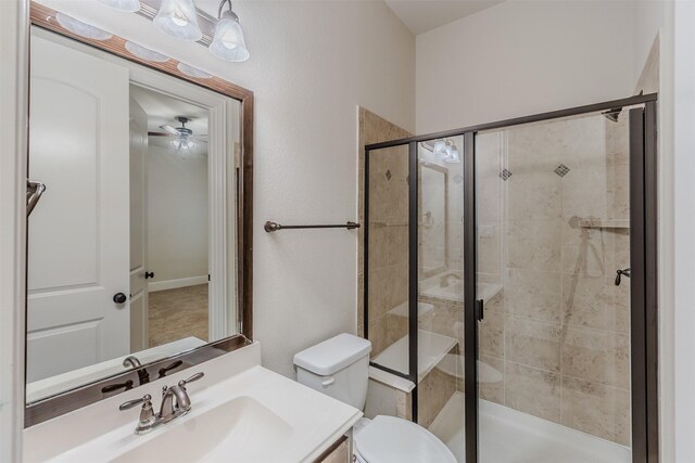 bathroom with vanity, toilet, a shower with shower door, and ceiling fan