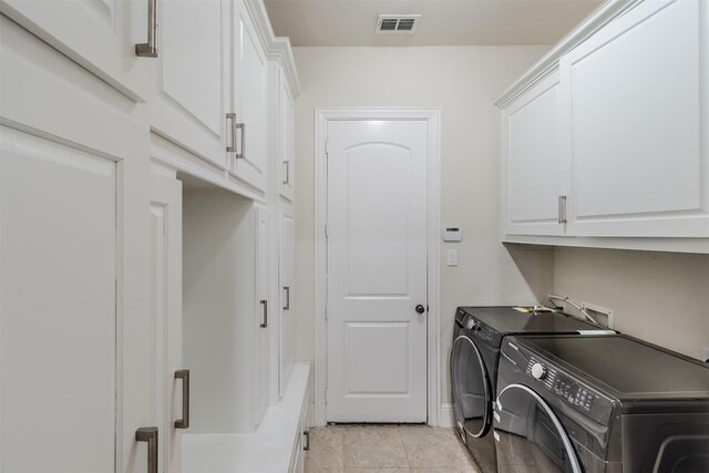 clothes washing area with washing machine and dryer, cabinets, and light tile patterned floors