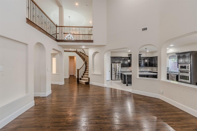 unfurnished living room with dark wood-type flooring, a notable chandelier, and a towering ceiling