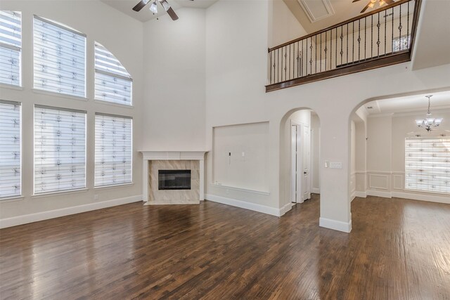 unfurnished living room featuring plenty of natural light, a high end fireplace, ceiling fan with notable chandelier, and dark hardwood / wood-style flooring