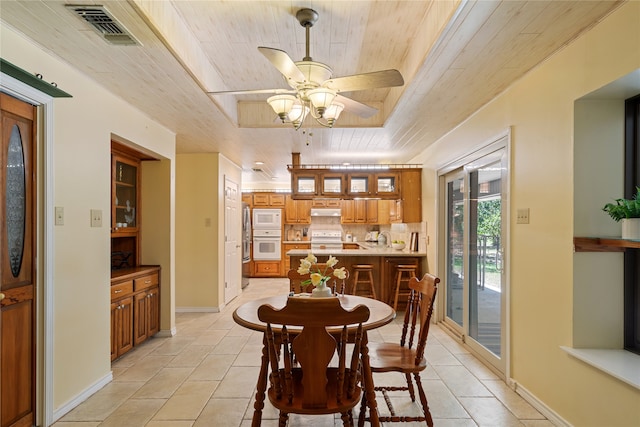 tiled dining room with a tray ceiling, wood ceiling, sink, and ceiling fan