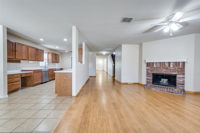 kitchen with dishwasher, a brick fireplace, light wood-type flooring, sink, and ceiling fan