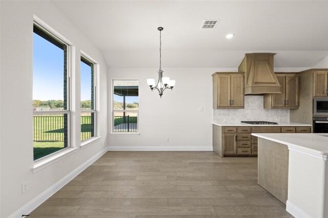 kitchen featuring hanging light fixtures, a healthy amount of sunlight, custom range hood, and light hardwood / wood-style floors