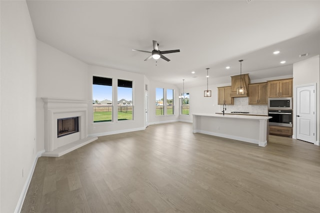 unfurnished living room with ceiling fan, sink, and light hardwood / wood-style floors