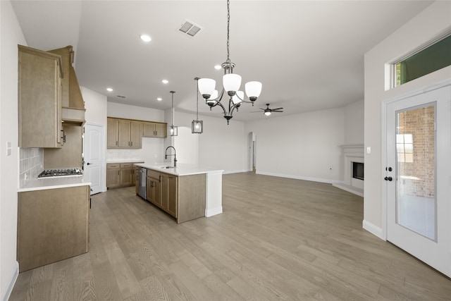 kitchen with light wood-type flooring, ceiling fan with notable chandelier, sink, decorative light fixtures, and a center island with sink