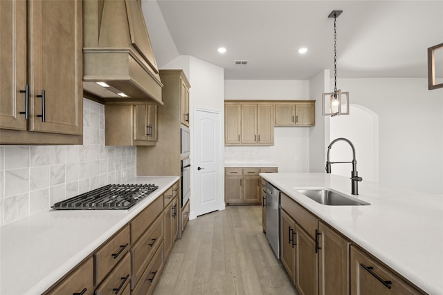 kitchen featuring appliances with stainless steel finishes, premium range hood, sink, light hardwood / wood-style flooring, and hanging light fixtures