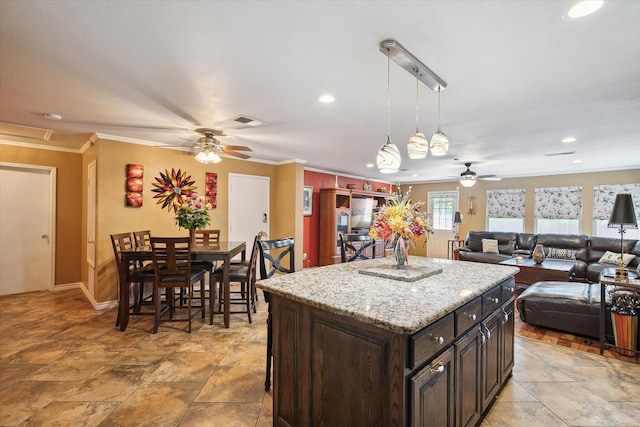 kitchen featuring dark brown cabinetry, a kitchen island, decorative light fixtures, ornamental molding, and a breakfast bar area