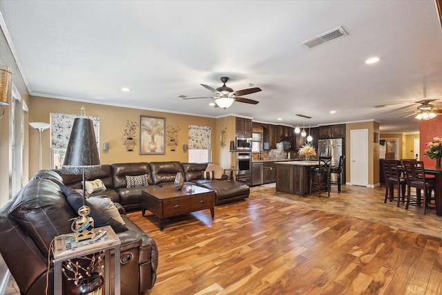 living room featuring ceiling fan, ornamental molding, and light hardwood / wood-style floors