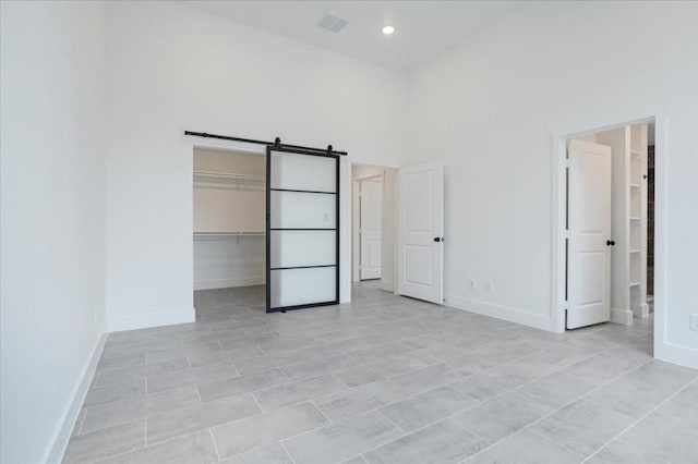 unfurnished bedroom with a towering ceiling, light tile patterned floors, a barn door, a spacious closet, and a closet