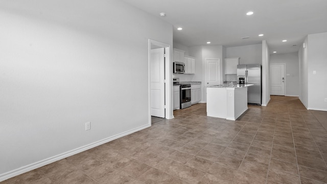 kitchen with an island with sink, stainless steel appliances, sink, white cabinetry, and light stone counters