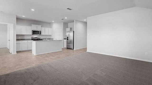 kitchen featuring white cabinets, appliances with stainless steel finishes, light colored carpet, lofted ceiling, and a center island with sink