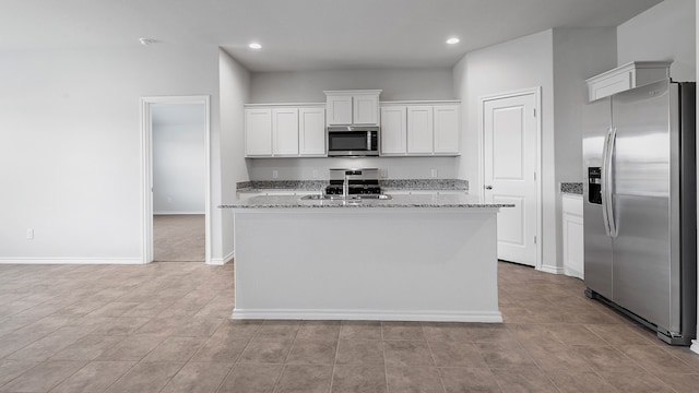 kitchen with a kitchen island with sink, sink, light stone countertops, appliances with stainless steel finishes, and white cabinets