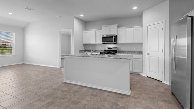 kitchen featuring light stone counters, stainless steel appliances, a center island with sink, and white cabinetry