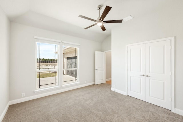 unfurnished bedroom featuring ceiling fan, a closet, light carpet, and vaulted ceiling