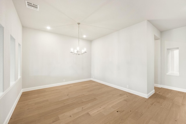 empty room with a notable chandelier and light hardwood / wood-style floors