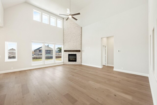 unfurnished living room featuring ceiling fan, light hardwood / wood-style floors, a fireplace, and high vaulted ceiling