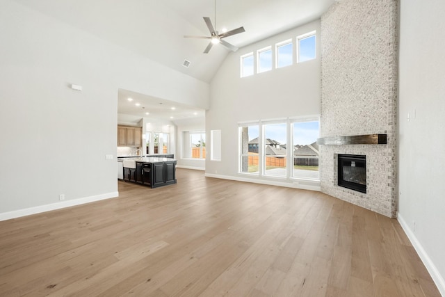 unfurnished living room with ceiling fan, a wealth of natural light, high vaulted ceiling, and a brick fireplace