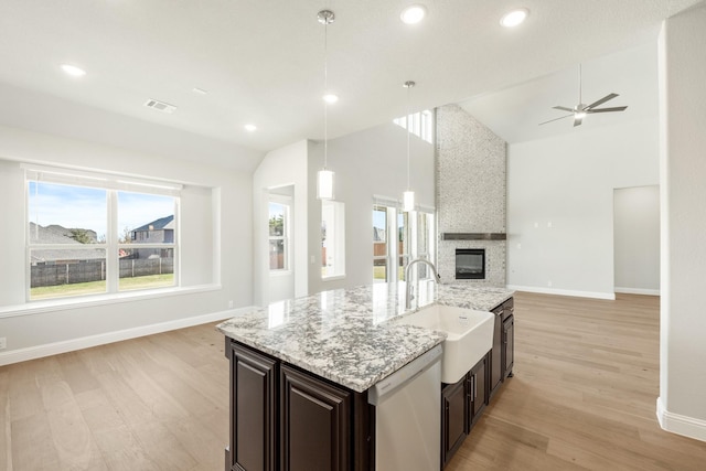 kitchen with sink, dishwasher, hanging light fixtures, dark brown cabinetry, and a center island with sink