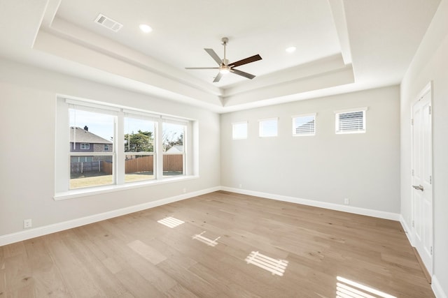 unfurnished room featuring a raised ceiling, ceiling fan, and light hardwood / wood-style floors