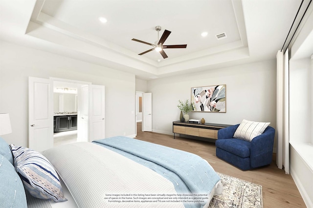 bedroom with a raised ceiling, ceiling fan, ensuite bathroom, and light wood-type flooring