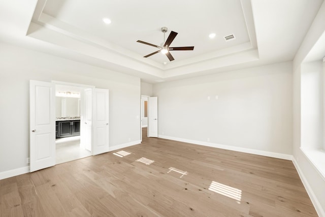 unfurnished bedroom with light wood-type flooring, a raised ceiling, ceiling fan, and connected bathroom