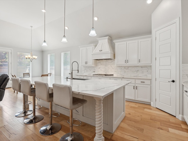 kitchen with a healthy amount of sunlight, custom exhaust hood, white cabinetry, and light hardwood / wood-style floors