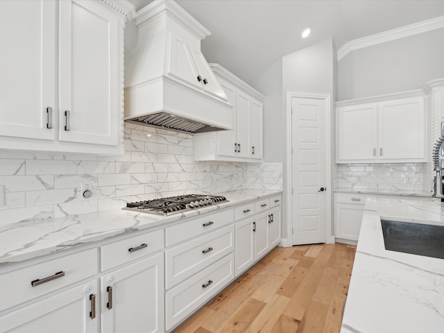 kitchen with light hardwood / wood-style flooring, stainless steel gas stovetop, premium range hood, crown molding, and white cabinetry