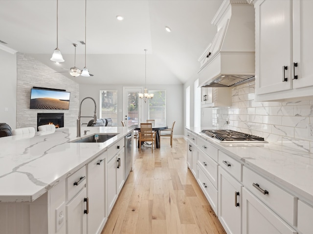 kitchen with vaulted ceiling, a stone fireplace, an island with sink, hanging light fixtures, and sink