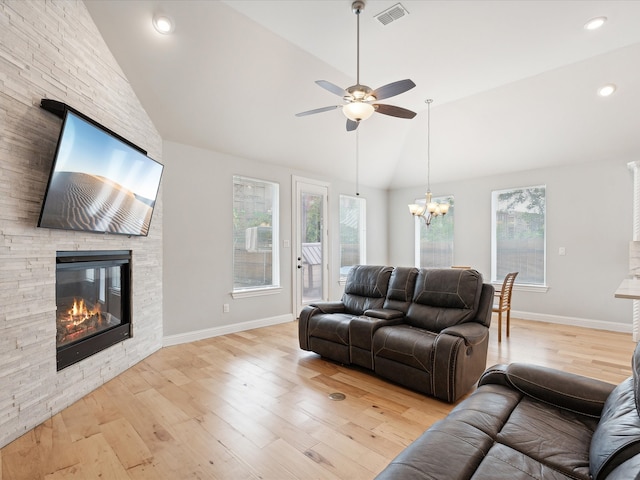 living room featuring lofted ceiling, ceiling fan with notable chandelier, a stone fireplace, and light hardwood / wood-style floors