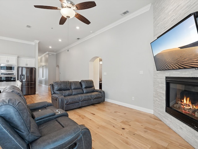 living room featuring light wood-type flooring, ceiling fan, a fireplace, and crown molding