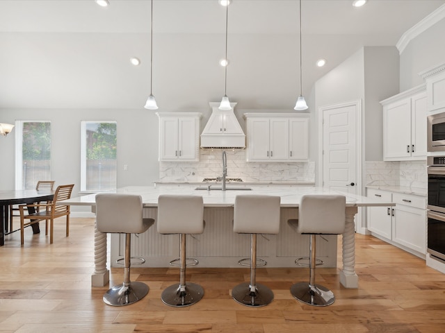 kitchen with a kitchen island with sink, pendant lighting, backsplash, and light hardwood / wood-style floors