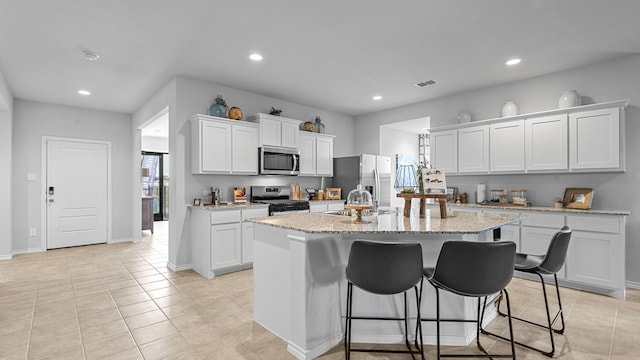 kitchen featuring a kitchen island with sink, light stone counters, stainless steel appliances, and white cabinets