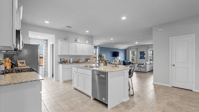 kitchen featuring a kitchen island with sink, stainless steel appliances, light stone counters, sink, and white cabinets