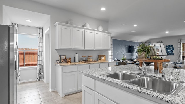 kitchen featuring white cabinets, light stone counters, sink, light tile patterned flooring, and stainless steel refrigerator with ice dispenser