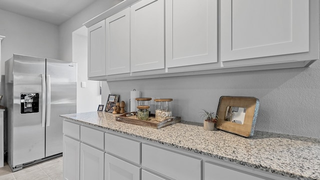 kitchen with stainless steel refrigerator with ice dispenser, white cabinetry, light stone counters, and light tile patterned flooring