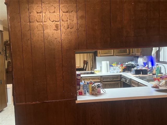 kitchen featuring kitchen peninsula, wood walls, black dishwasher, and sink