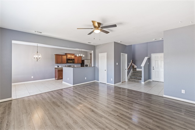 unfurnished living room featuring light wood-type flooring and ceiling fan with notable chandelier