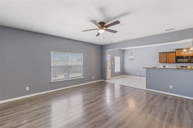 unfurnished living room featuring light hardwood / wood-style floors, ceiling fan with notable chandelier, and a textured ceiling