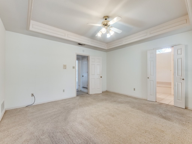 unfurnished bedroom featuring light carpet, a tray ceiling, ceiling fan, and ensuite bathroom