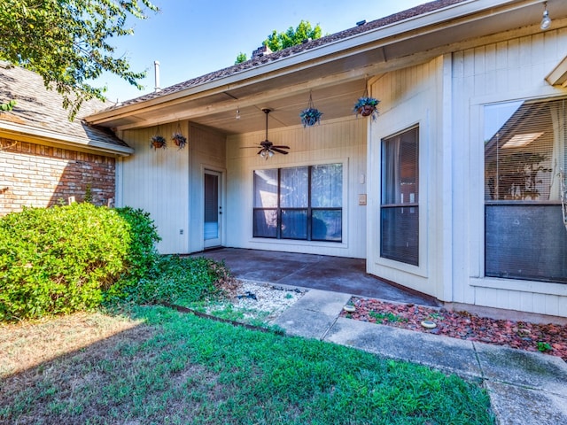 view of exterior entry featuring a lawn, ceiling fan, and a patio