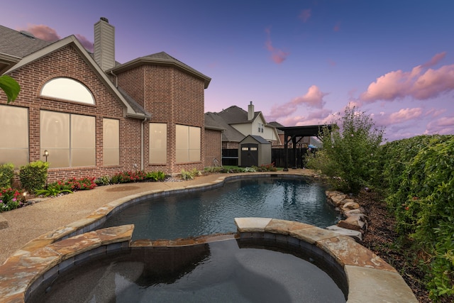 pool at dusk featuring an in ground hot tub