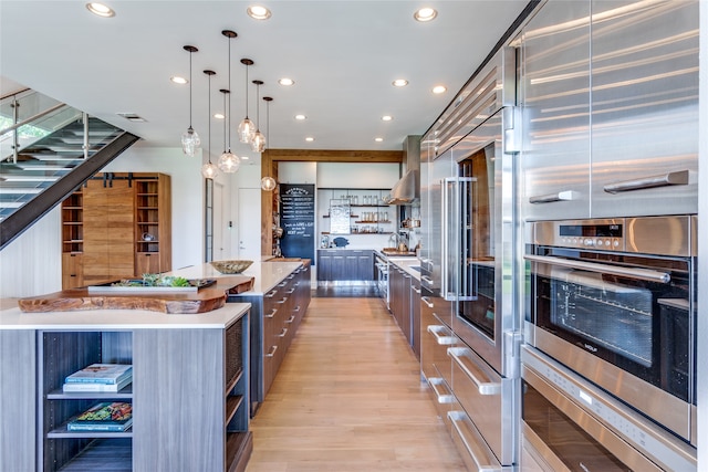 kitchen with decorative light fixtures, a spacious island, range hood, stainless steel double oven, and light wood-type flooring