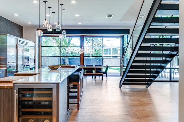 bar with beverage cooler, an inviting chandelier, light hardwood / wood-style floors, and a healthy amount of sunlight